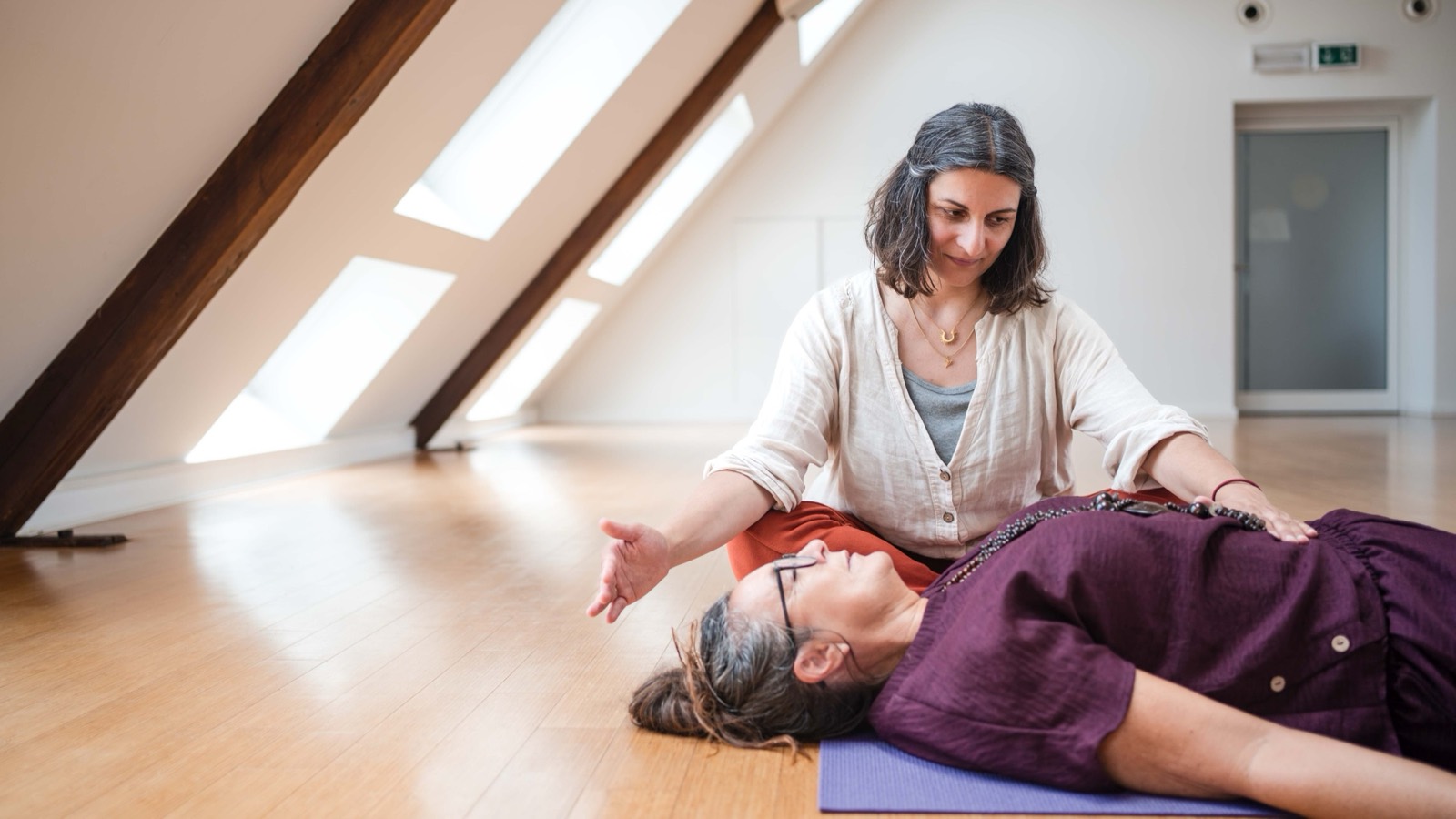 Breathwork-Session im Dachstudio: Jennifer kniet neben einer liegenden Teilnehmerin und hält die Hand über ihr